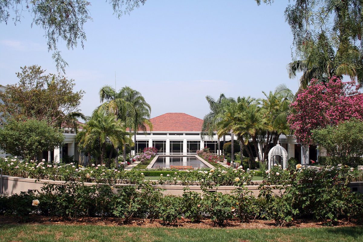 Rose beds and a long reflecting pool leading to a red-roofed, white-columned building framed by palms at the Richard Nixon Presidential Library gardens